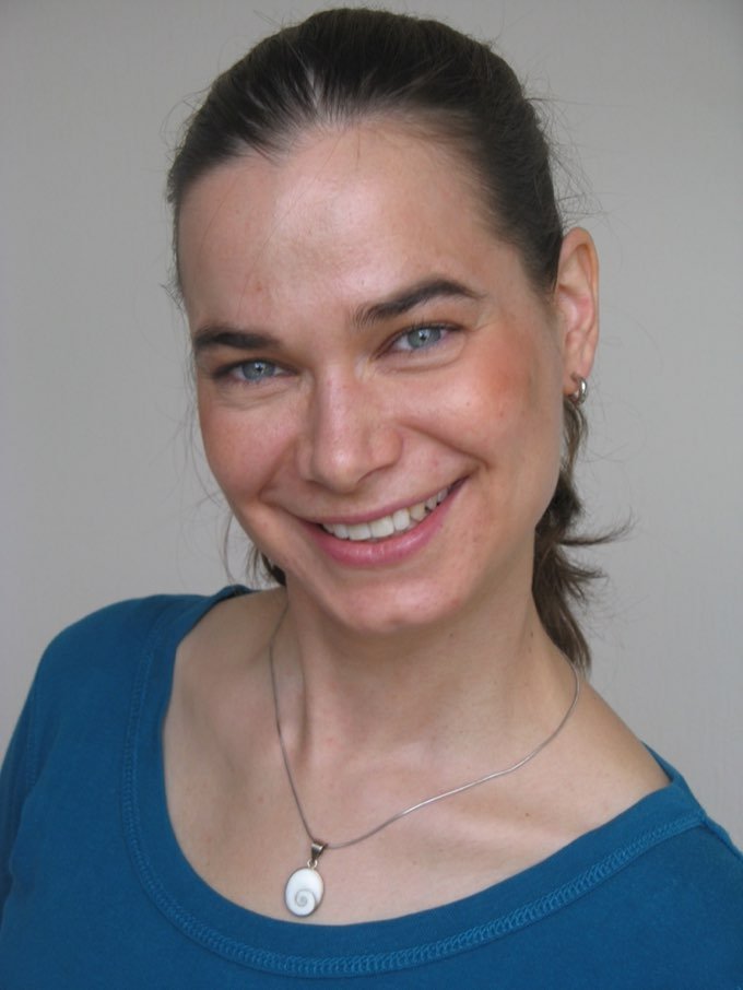 Tanja Thomira Drees, lächelnd, dunkle zurückgebundene Haare, türkisfarbenes Oberteil und eine Kette mit einem spiralförmigen Anhänger